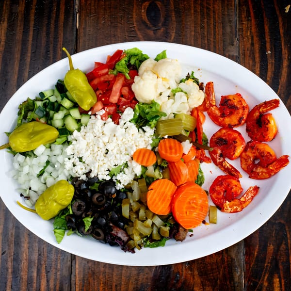 A Gyro Guys platter with grilled shrimp, feta, olives, pickled vegetables, and fresh salad.