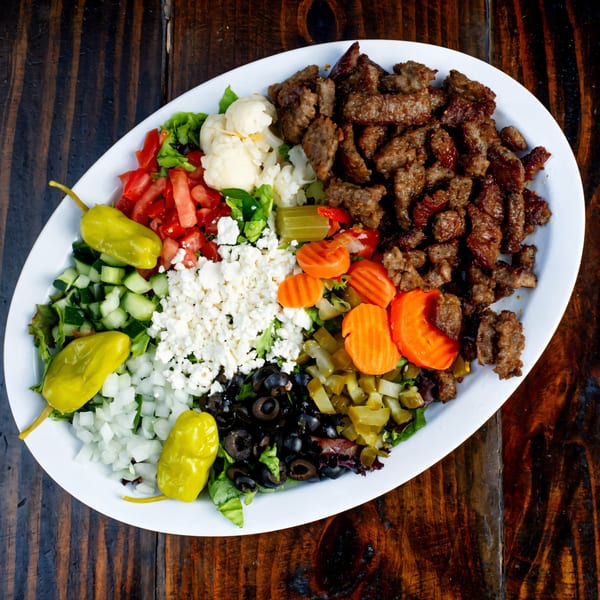 Gyro Guys' gyro plate with meat, lettuce, tomatoes, cucumbers, feta, olives, carrots, and peppers.