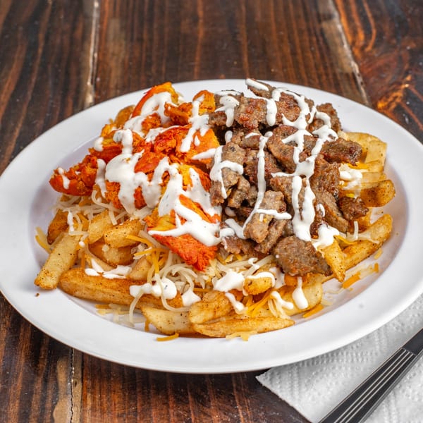 Gyro Guys' fries topped with chicken, beef, shredded cheese, and white sauce on a white plate.